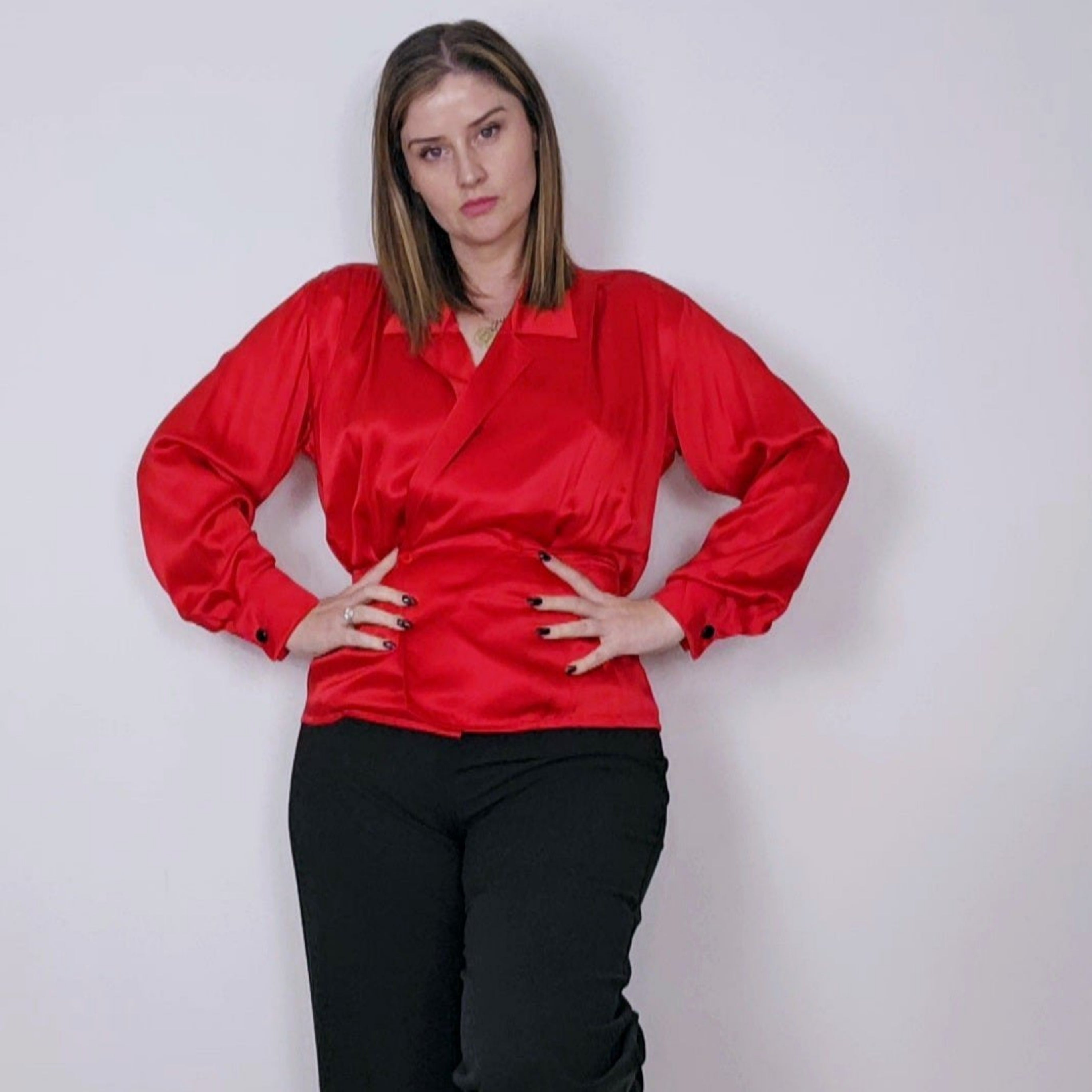 A woman standing, wearing a red silk blouse with black square buttons on the sleeves and a cinched waist. The blouse features a double-breasted style with red buttons and hidden snap buttons.
