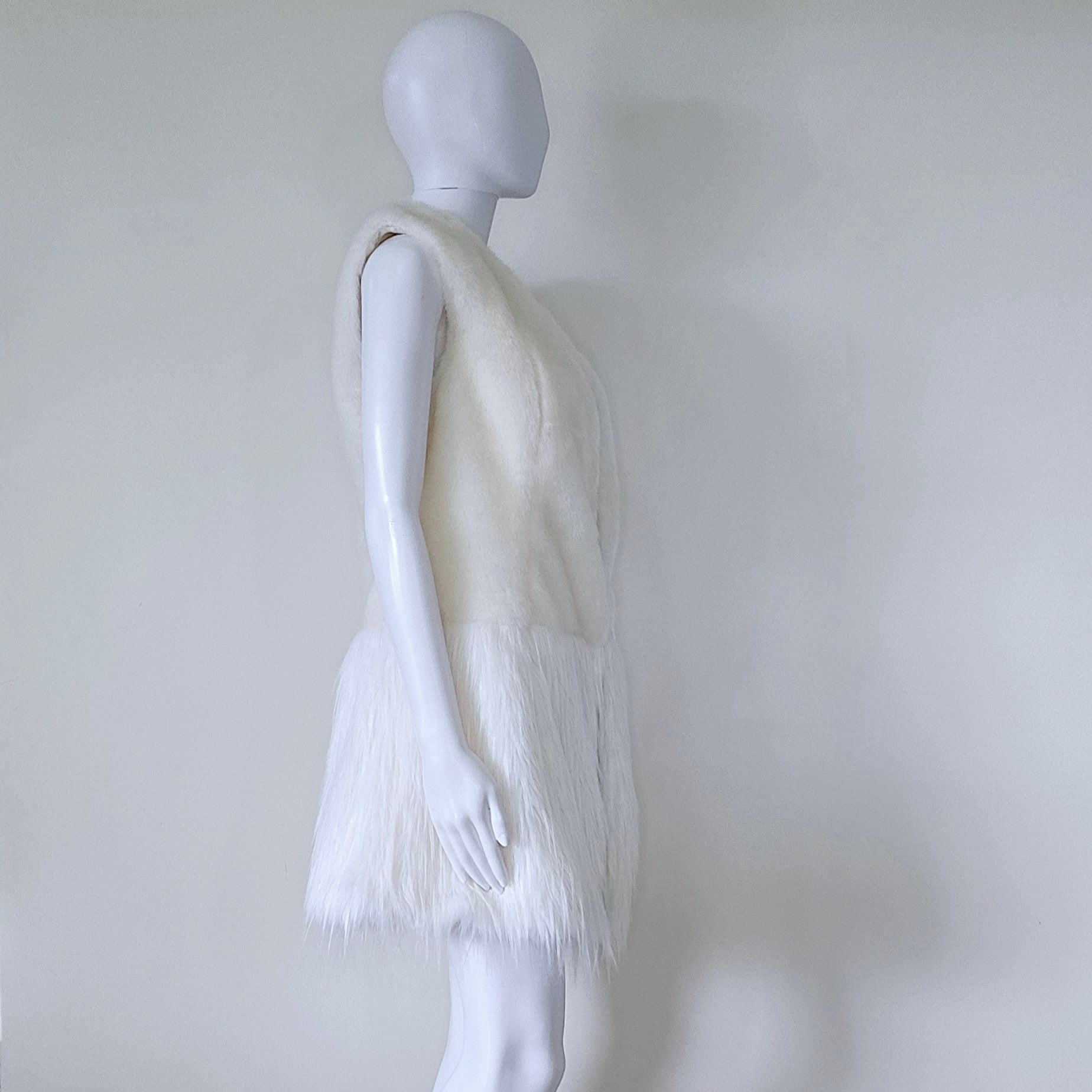 Mannequin wearing a white dress with fringe details against a plain background