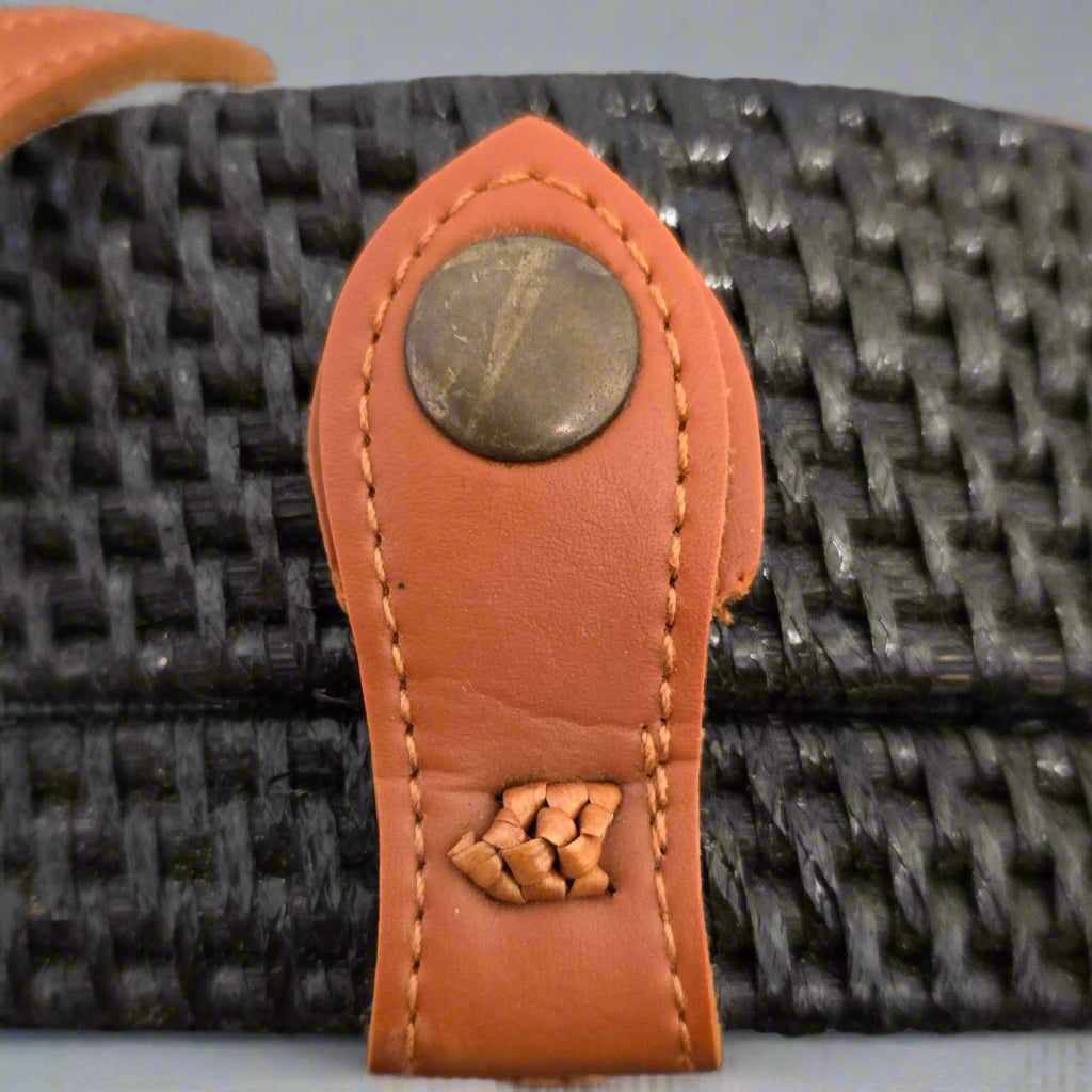 Close-up of a textured strap with a brown leather tab and metal buckle on a gray background.
