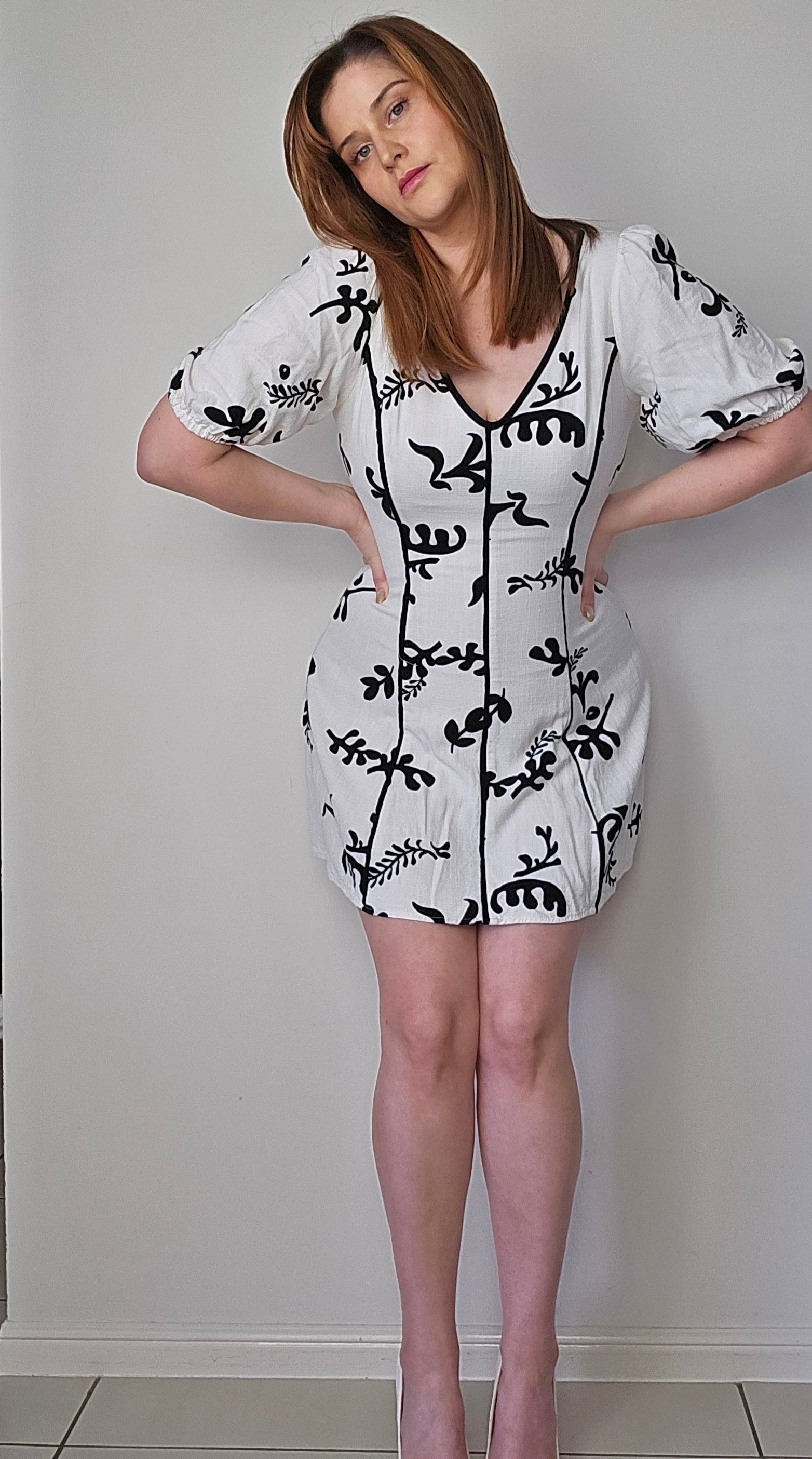 A woman modeling a black and white linen mini dress with puff sleeves and a v-neckline.