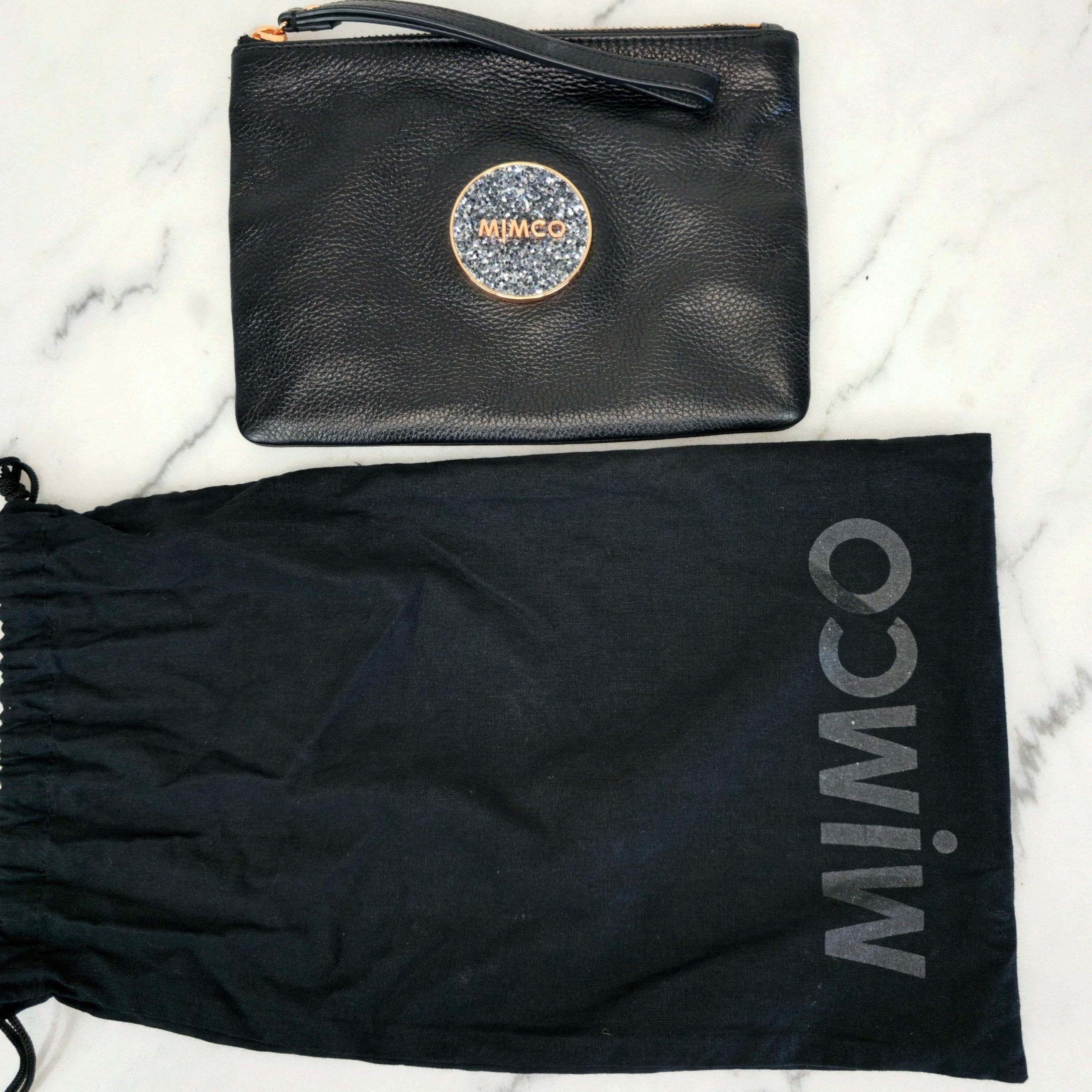 Black pouch with glittery logo and matching drawstring bag on a marble background