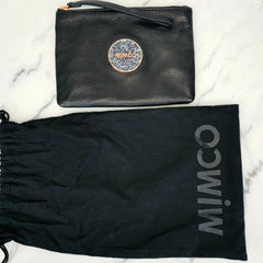 Black pouch with glittery logo and matching drawstring bag on a marble background