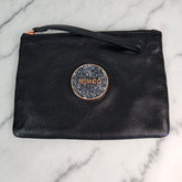 A black leather clutch pouch with rose gold accents, featuring the Mimco logo in a rose gold circular frame with a wrist strap on top.