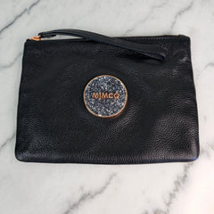 A black leather clutch pouch with rose gold accents, featuring the Mimco logo in a rose gold circular frame with a wrist strap on top.