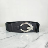 A black belt with a silver-tone circular buckle, designed with horizontal pleats, placed on a marble surface.