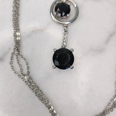 A silver multi-chain necklace with three round drops featuring black gemstones and rhinestone accents on a white background.