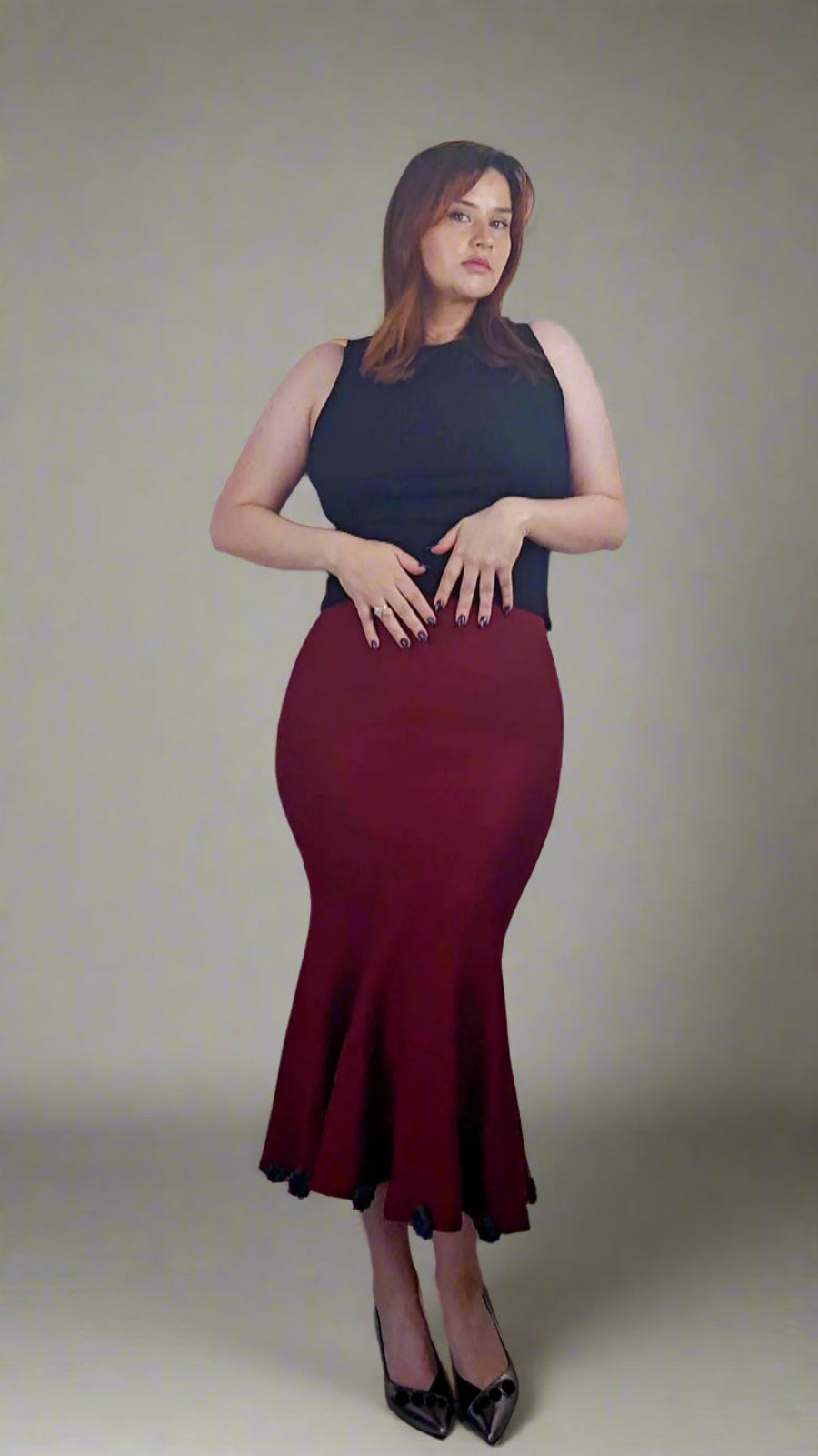 A person wearing a deep red knit skirt with a black floral pattern, reaching up to the thighs, paired with a black top and black shoes. The image shows only the lower half of the person's body, from the waist down.