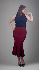 Woman wearing a black top and maroon skirt against a plain background