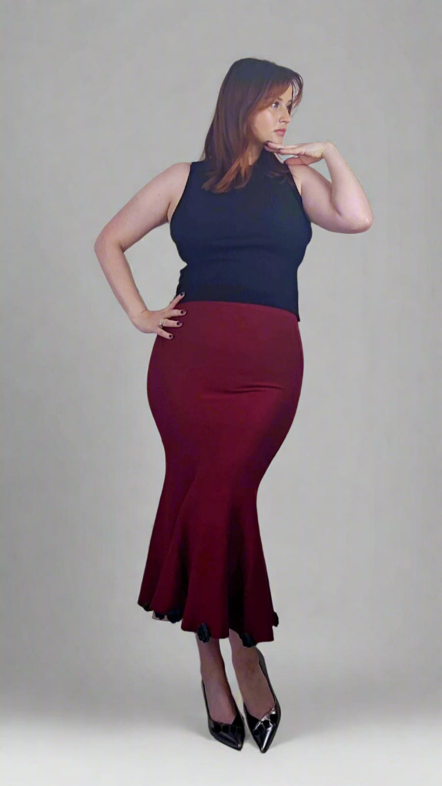 Woman wearing a black sleeveless top and burgundy skirt against a gray background