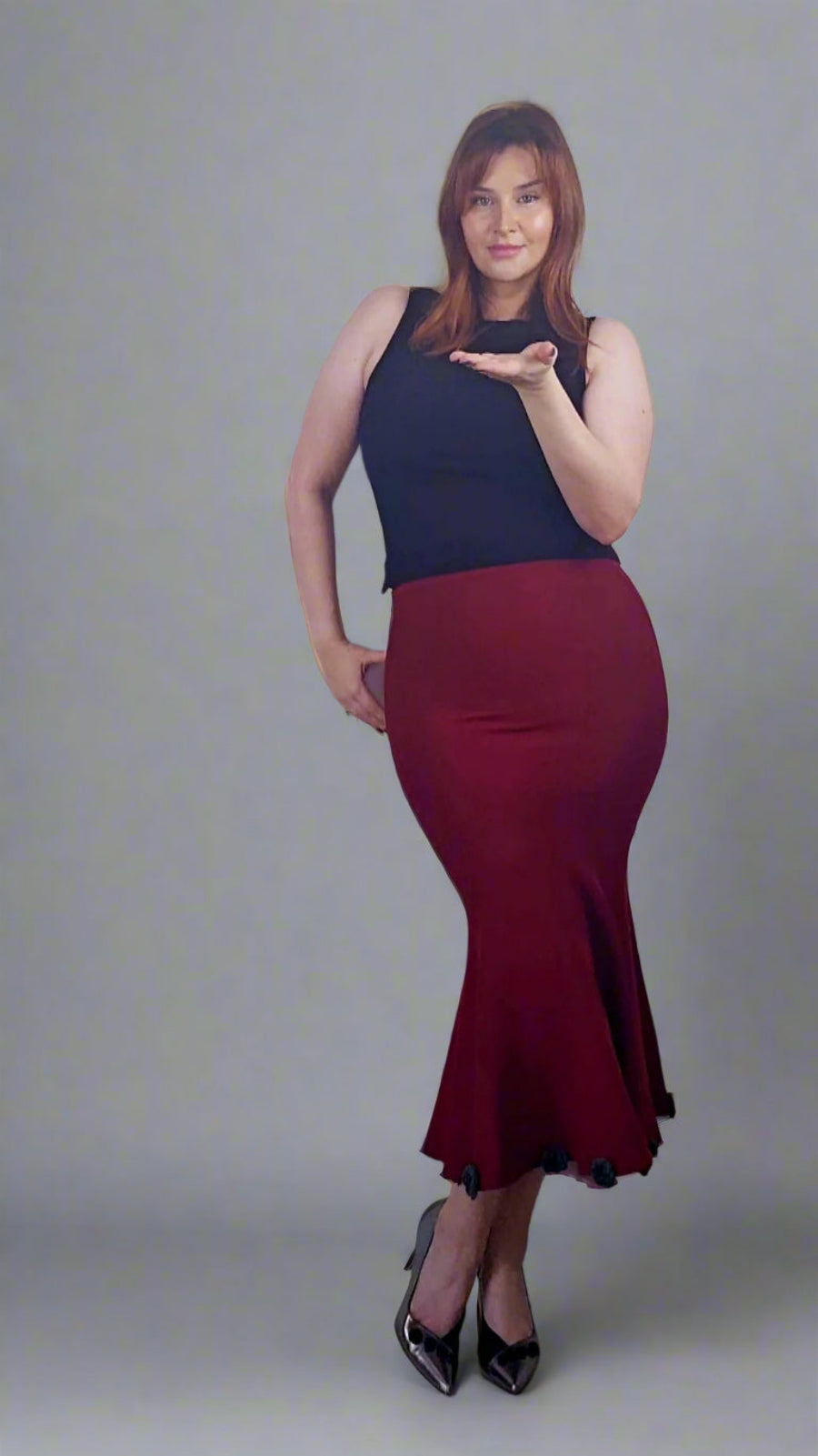 Woman wearing a black top and red skirt against a white wall.