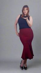 Woman wearing a black top and red skirt against a white wall.