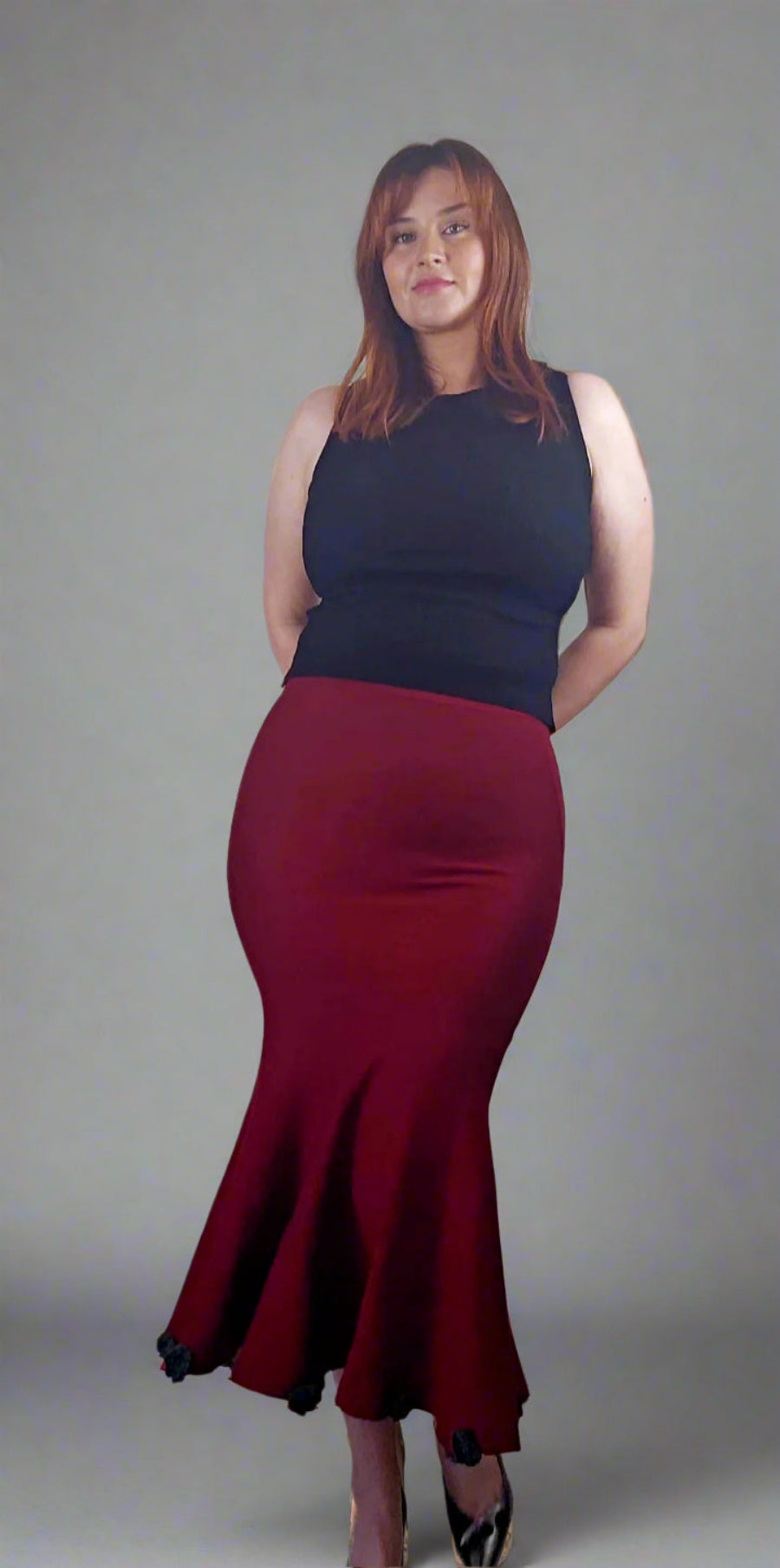Woman wearing a black top and red skirt against a gray background