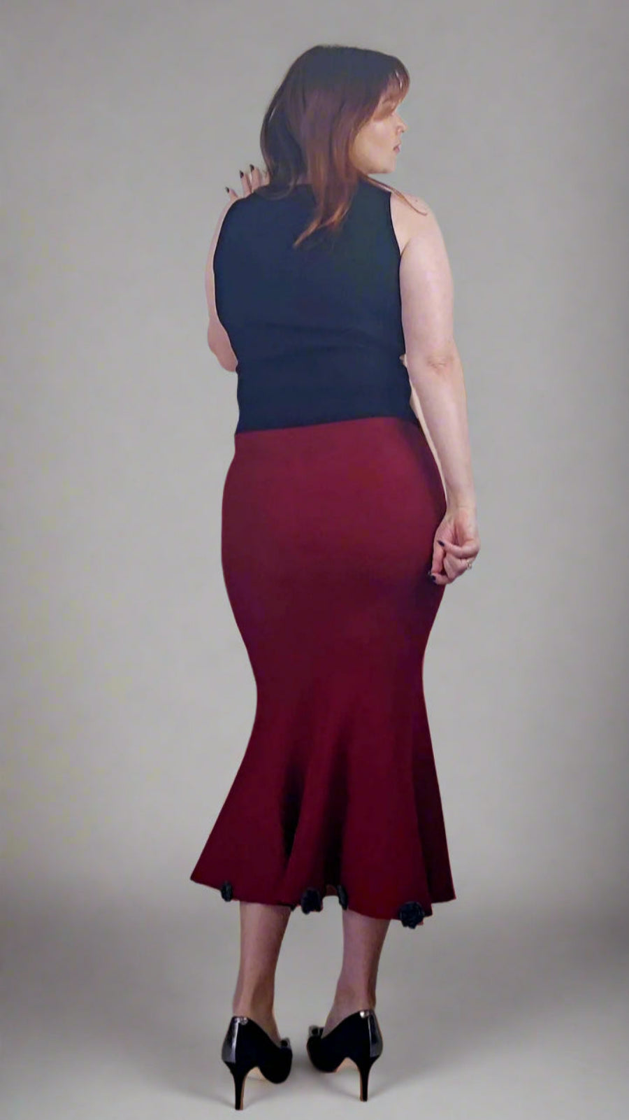 Woman wearing a navy top and burgundy skirt against a plain background