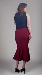 Woman wearing a navy top and burgundy skirt against a plain background