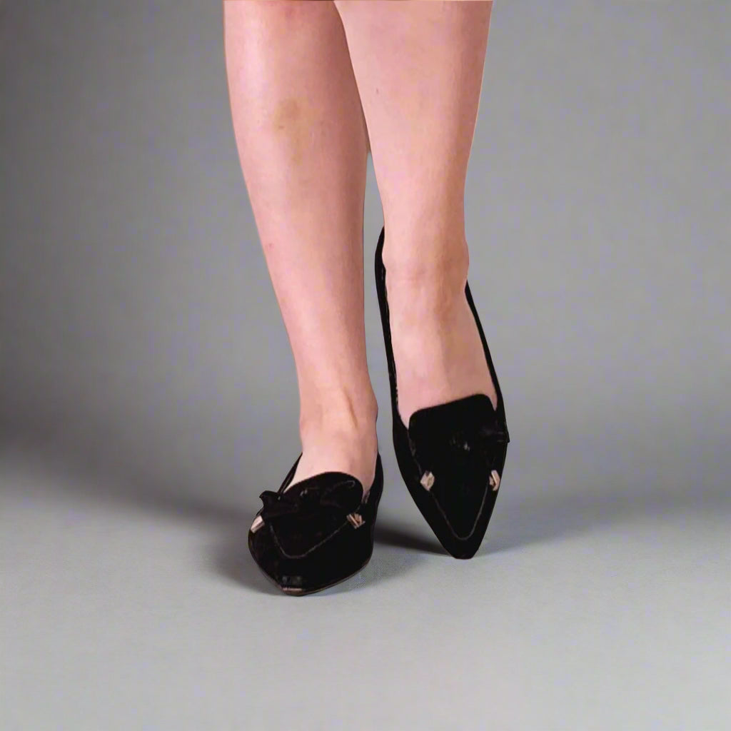 Person wearing black pointed-toe shoes on a white floor.