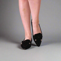 Person wearing black pointed-toe shoes on a white floor.