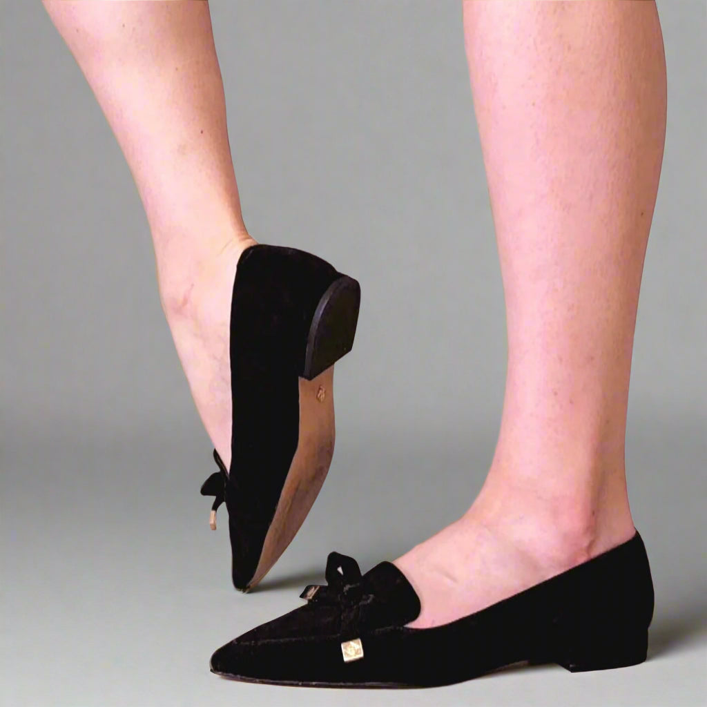 Black loafers with bow details worn by a person on a light background