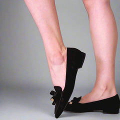 Black flats with bow details worn by a person on a light background