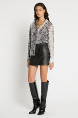 Woman wearing a patterned blouse, black leather skirt, and black boots on a white background