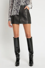 Person wearing a black leather mini skirt and black patent knee-high boots on a white background