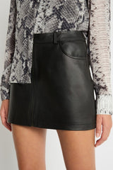 Black leather skirt worn with a patterned top on a neutral background