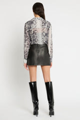 Person wearing a patterned blouse, black leather skirt, and black high-heeled boots on a white background