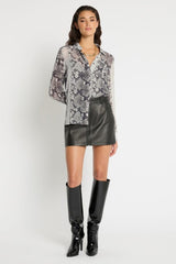 Woman wearing a patterned blouse, leather shorts, and black knee-high boots on a white background