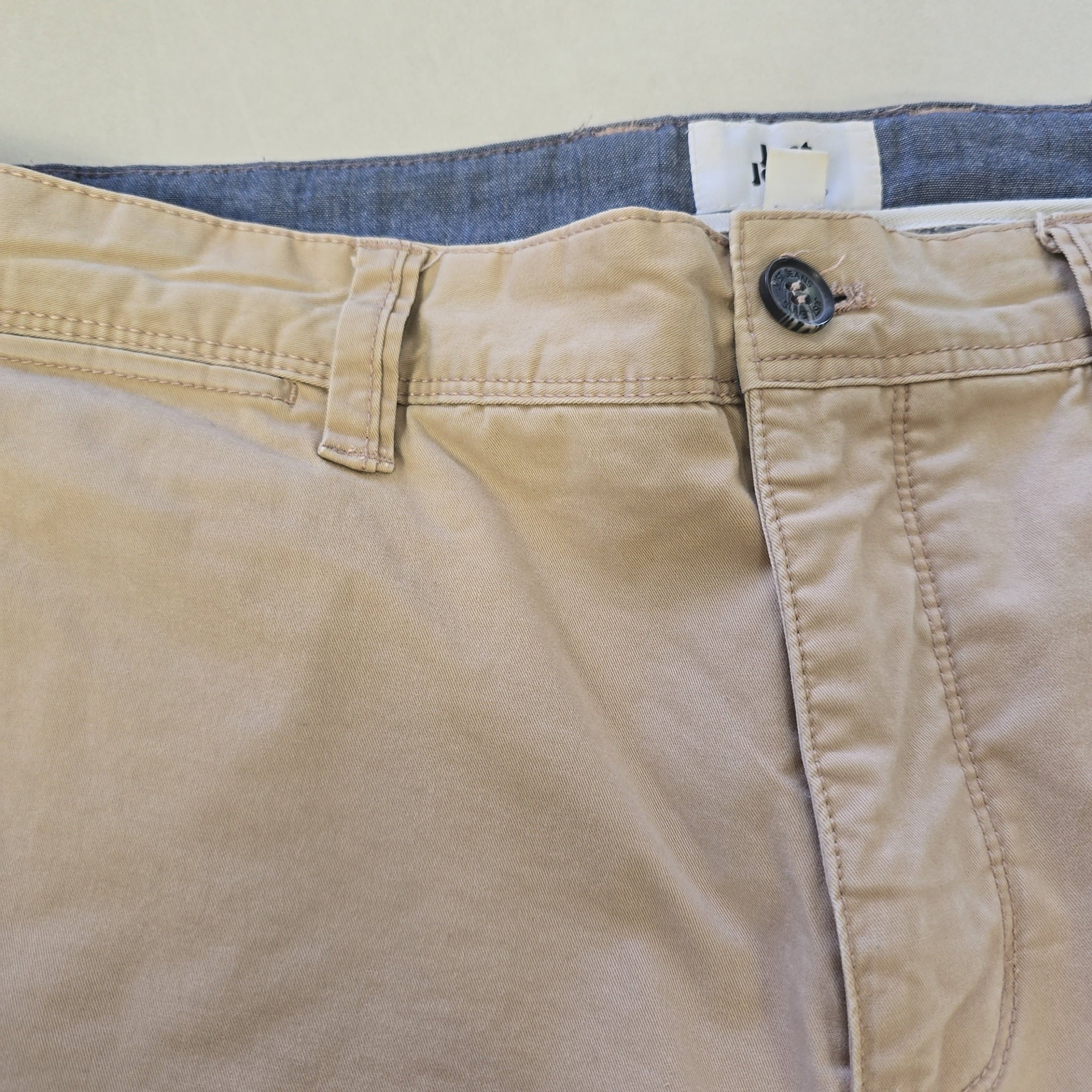 Close-up of beige pants with a visible brand tag on a neutral background