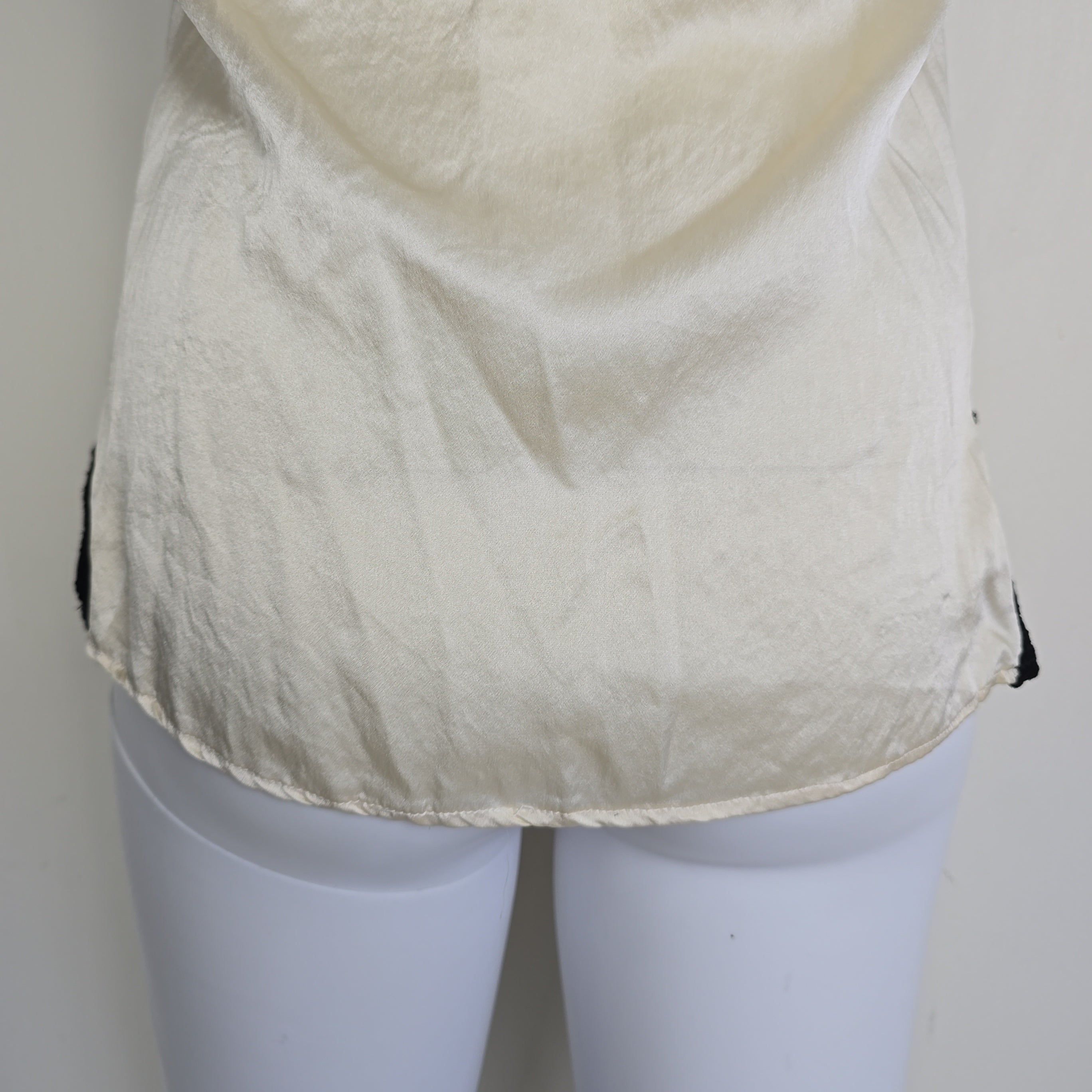 Mannequin wearing a white top with black lace details on a plain background