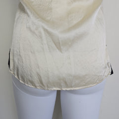 Mannequin wearing a white top with black lace details on a plain background