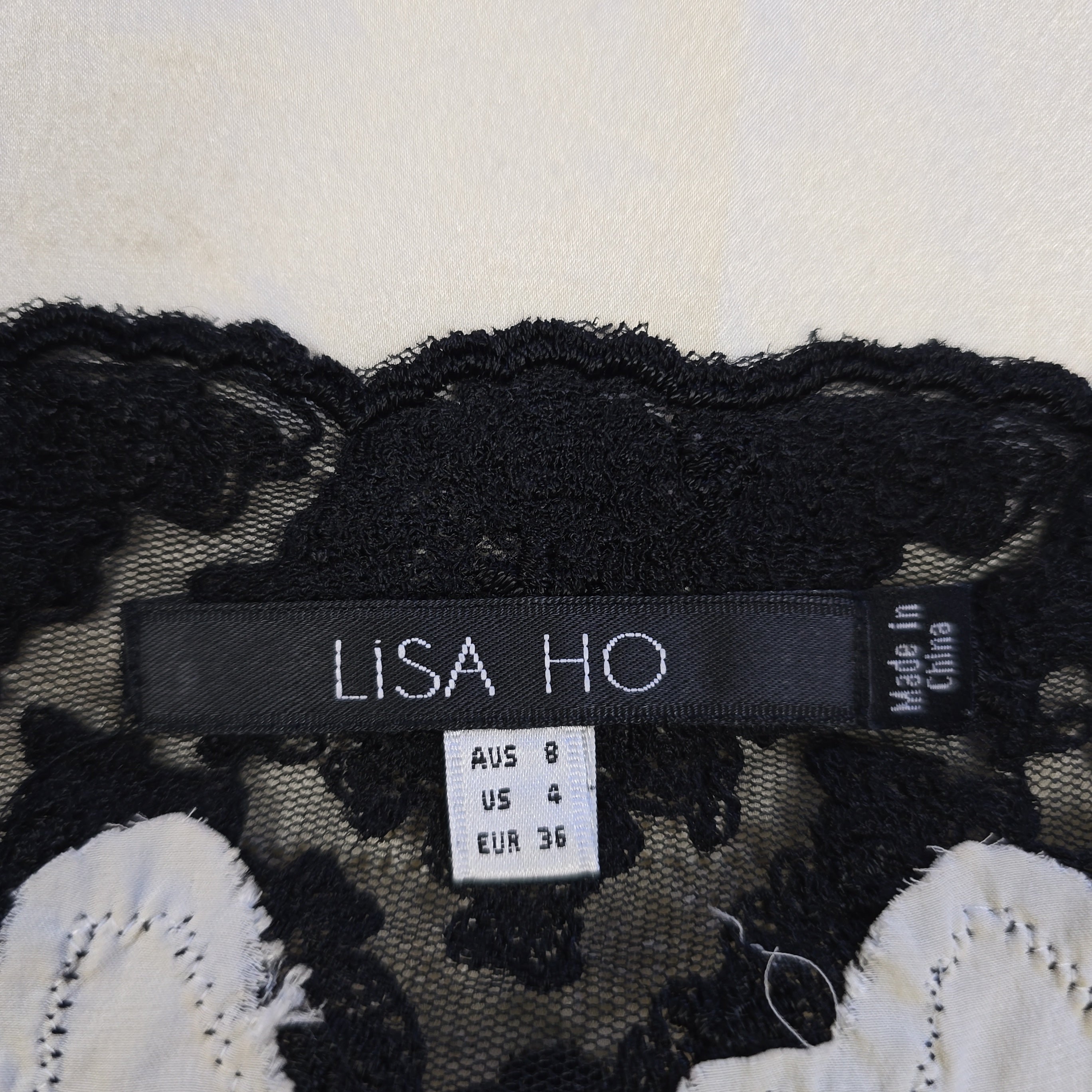 Close-up of a label on a black lace garment with floral details, featuring the brand 'Lisa Ho'.