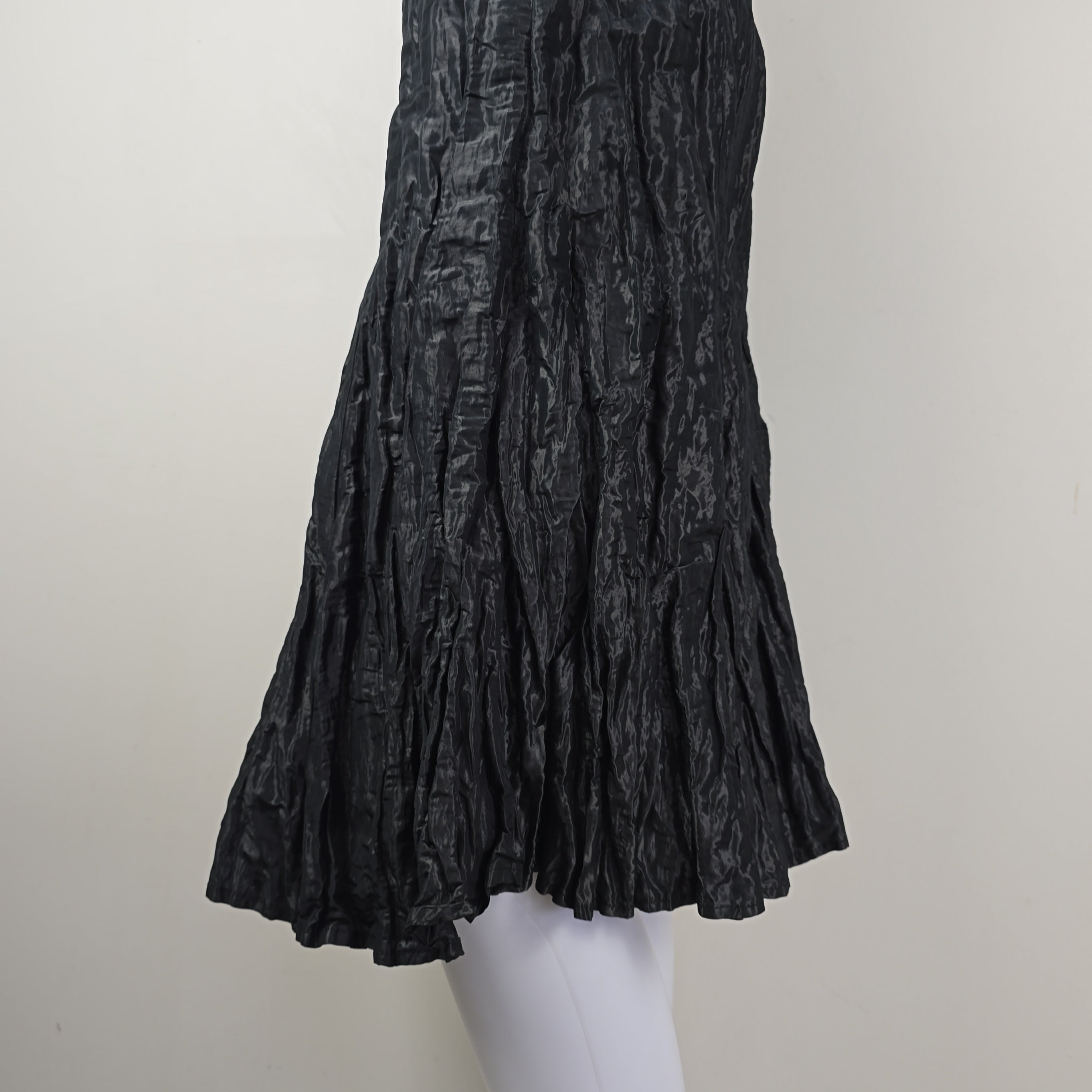 Black pleated skirt on a white mannequin arm against a light gray background