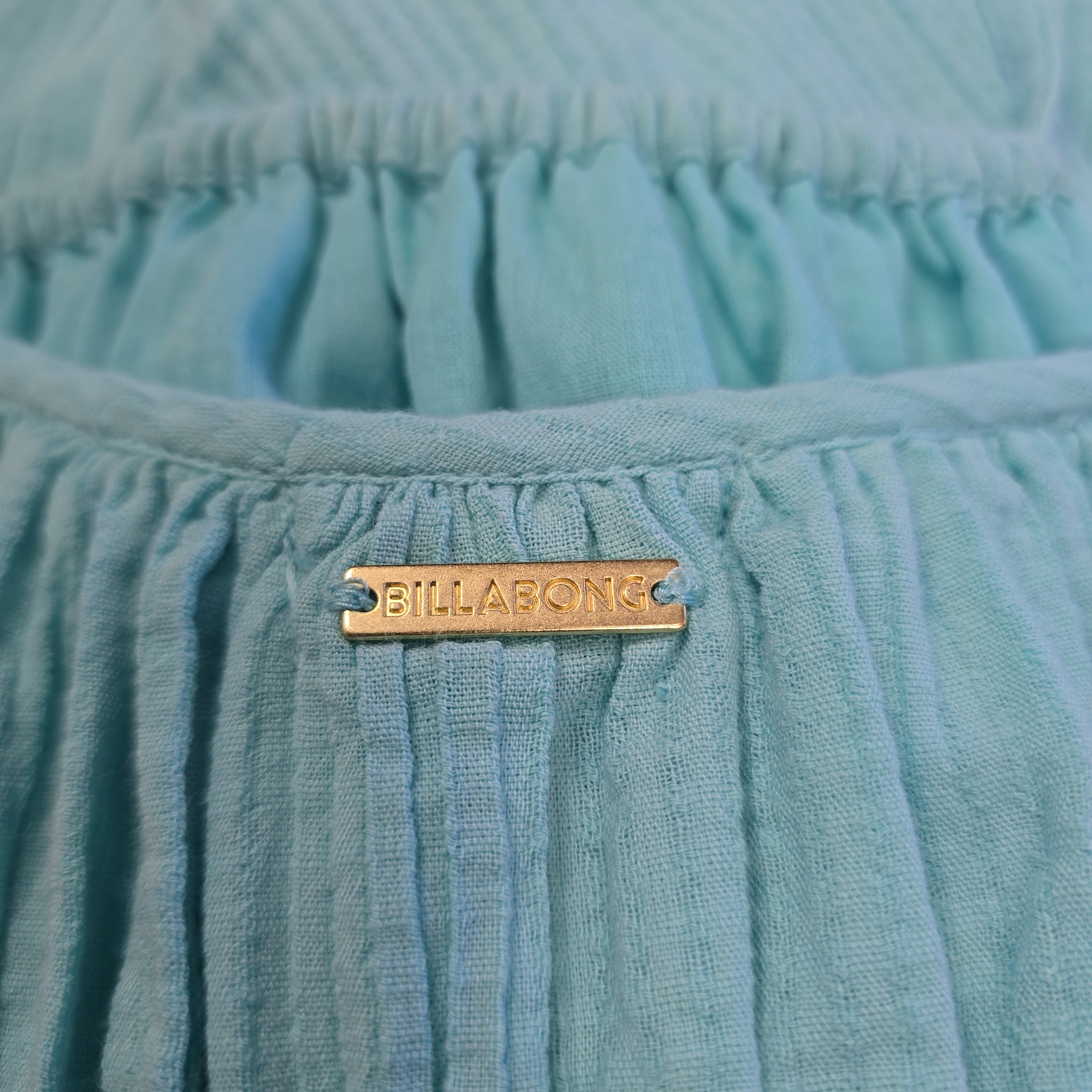Close-up of a teal textured fabric with a gold label on a matching background