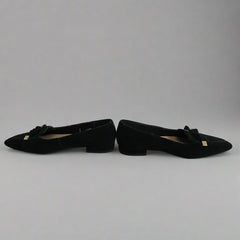 Black pointed-toe shoes with bow details leaning against a white wall.