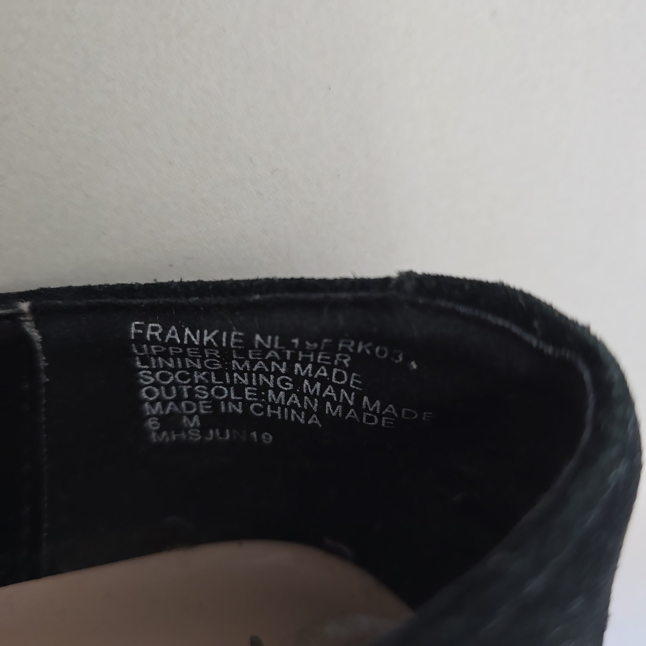 Close-up of a black shoe with brand and size information on a light gray background