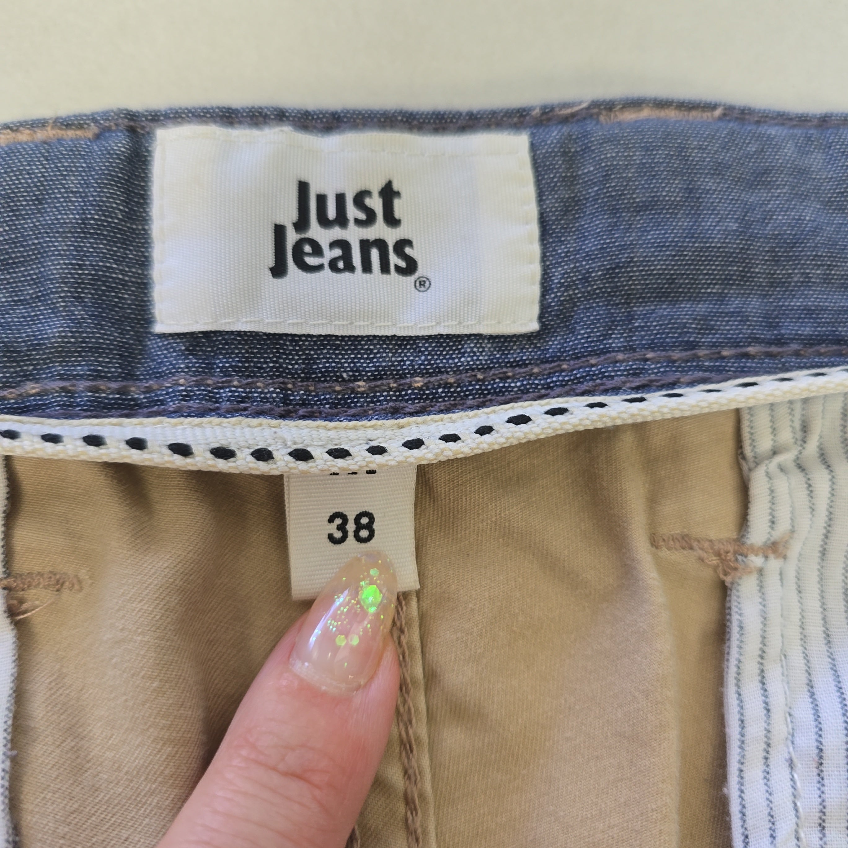 Close-up of a 'Just Jeans' label on a denim garment with a hand pointing to size 38.
