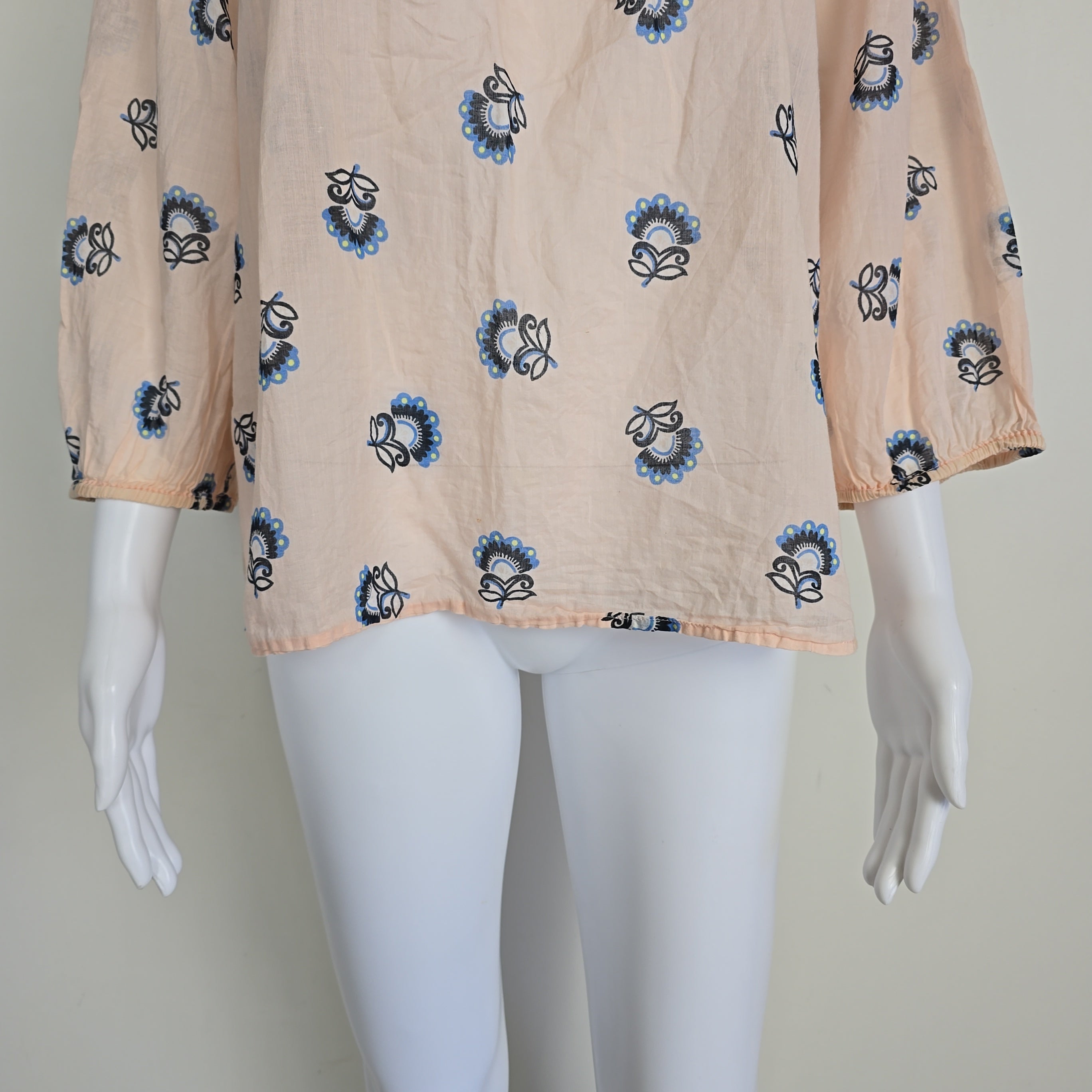 Mannequin draped with beige fabric featuring blue floral patterns on a plain background