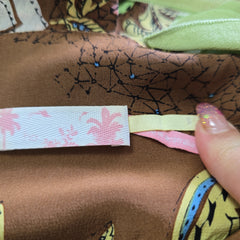 Close-up of a hand holding a floral ribbon with a brown fabric background