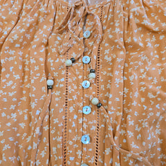Close-up of a peach-colored fabric with white floral pattern and buttons.