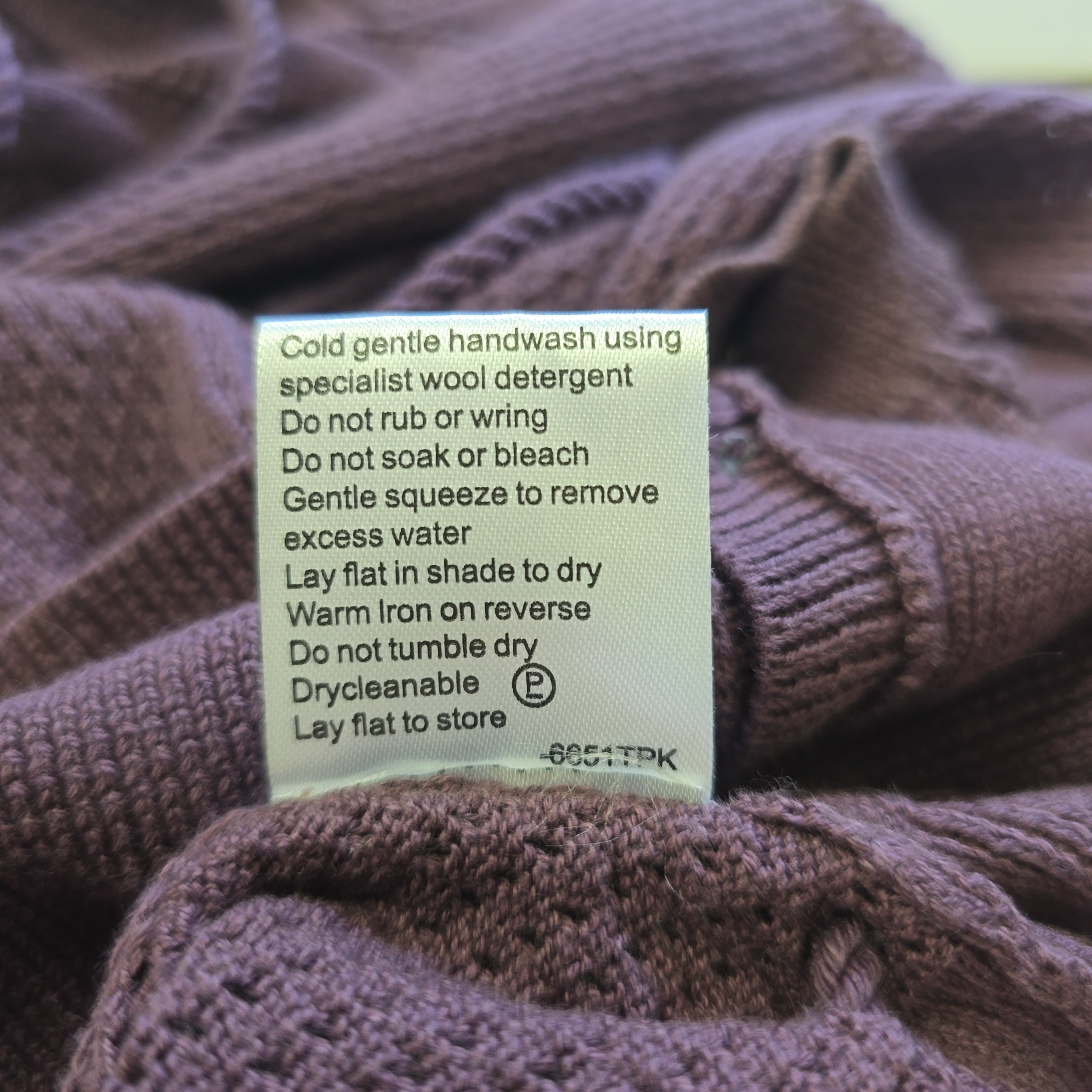 Close-up of a label on a purple knitted sweater with care instructions.