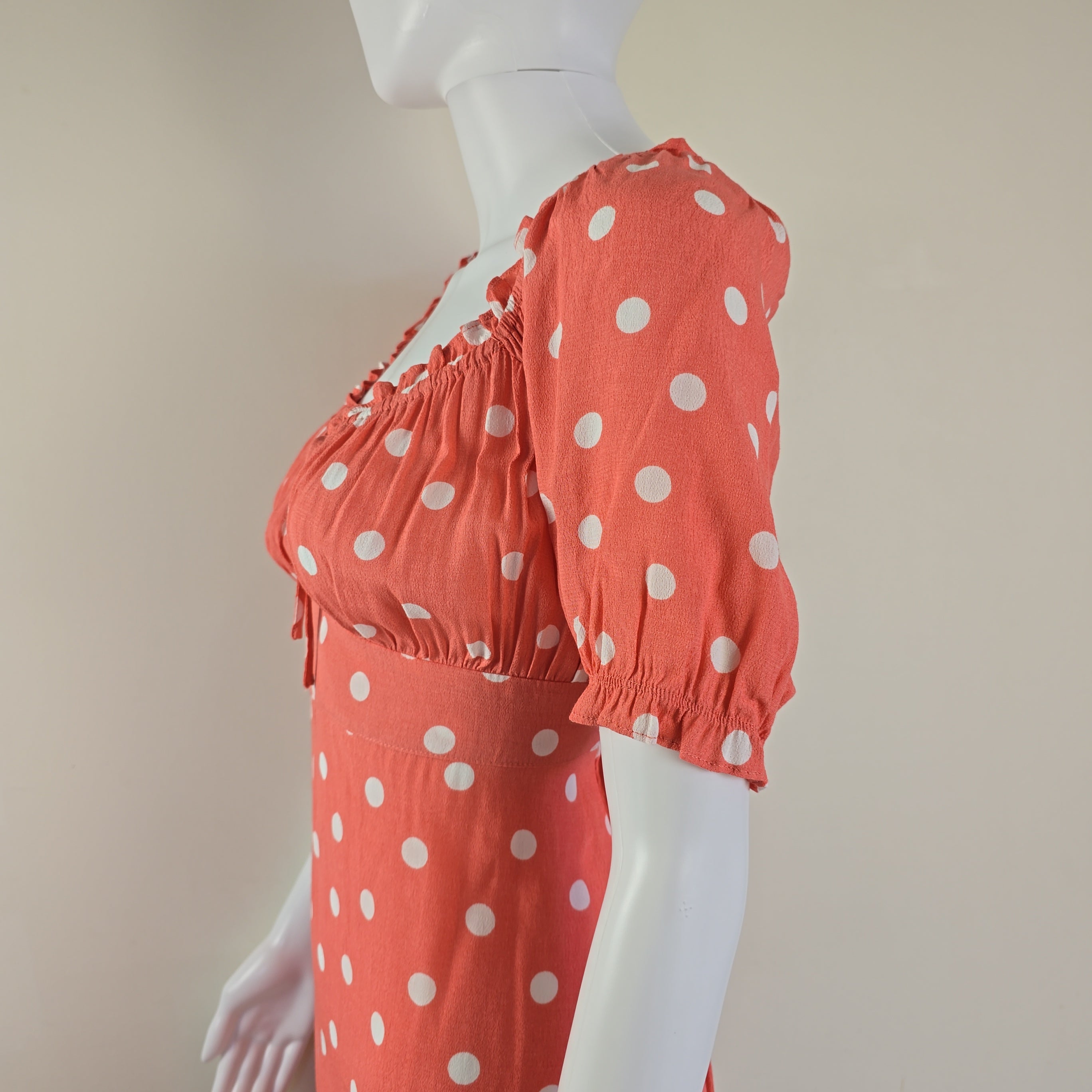 Coral polka dot dress on a mannequin against a beige background