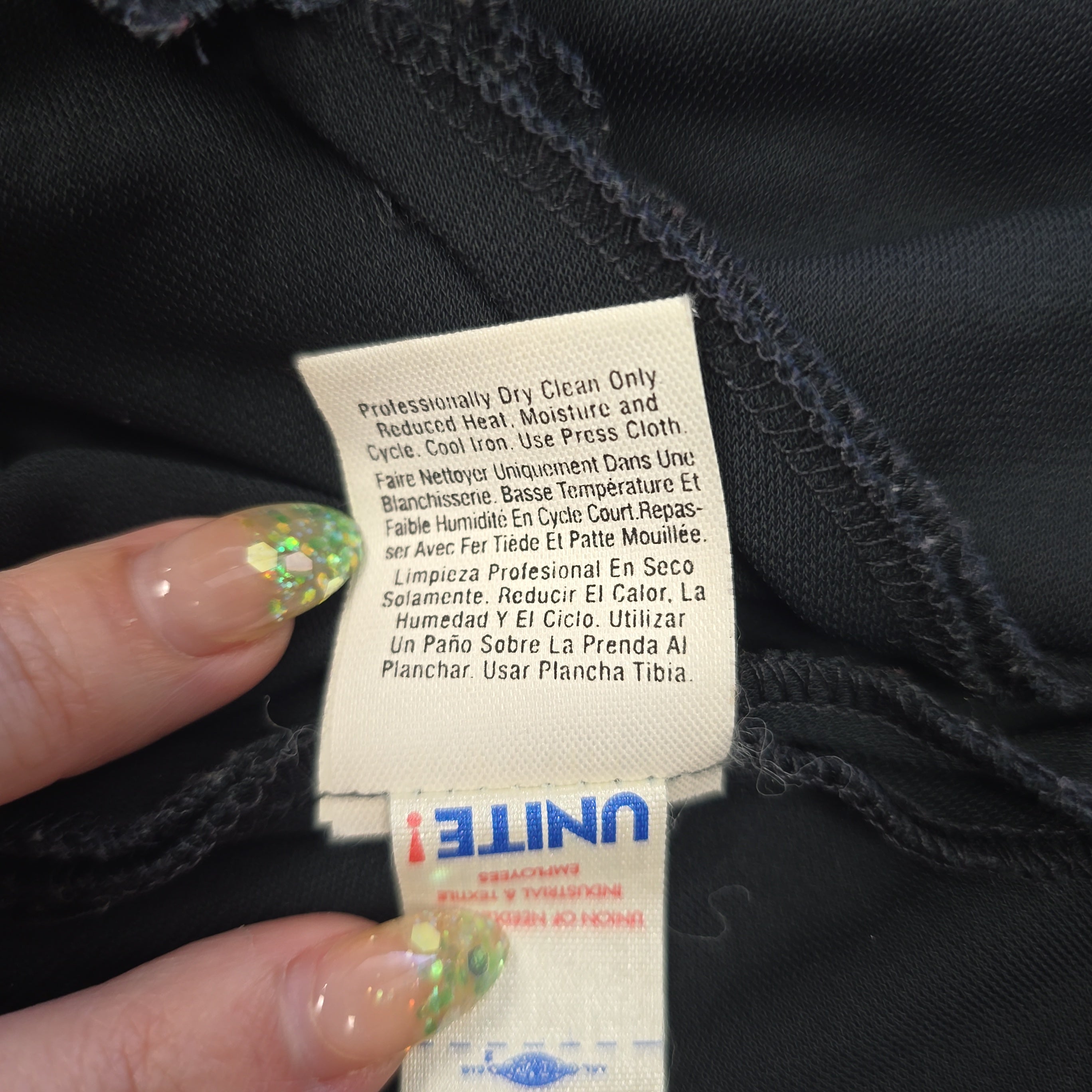 Close-up of a clothing tag on black fabric with a hand holding it.