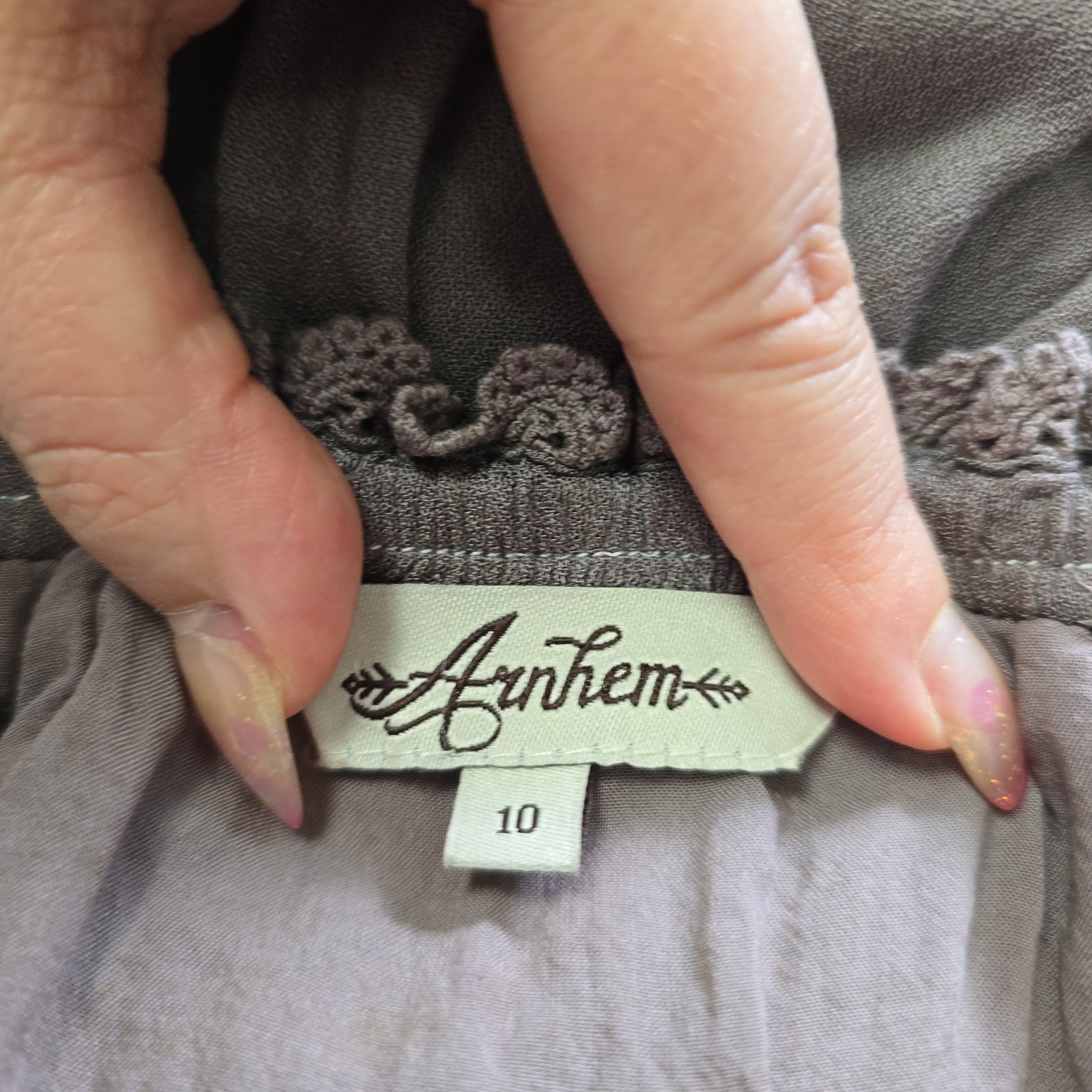 Hand holding a clothing tag with 'Anthem' brand name on a gray garment.