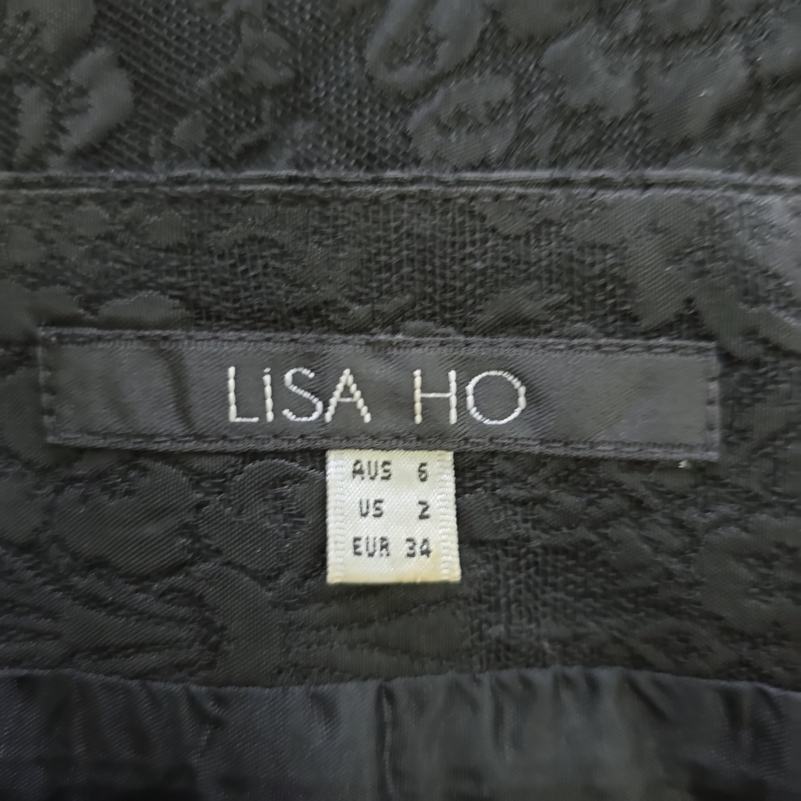 Close-up of a 'Lisa Ho' label on black textured fabric.