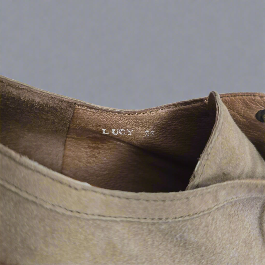 Close-up of a brown leather shoe with 'LUCY' branding on a blurred background