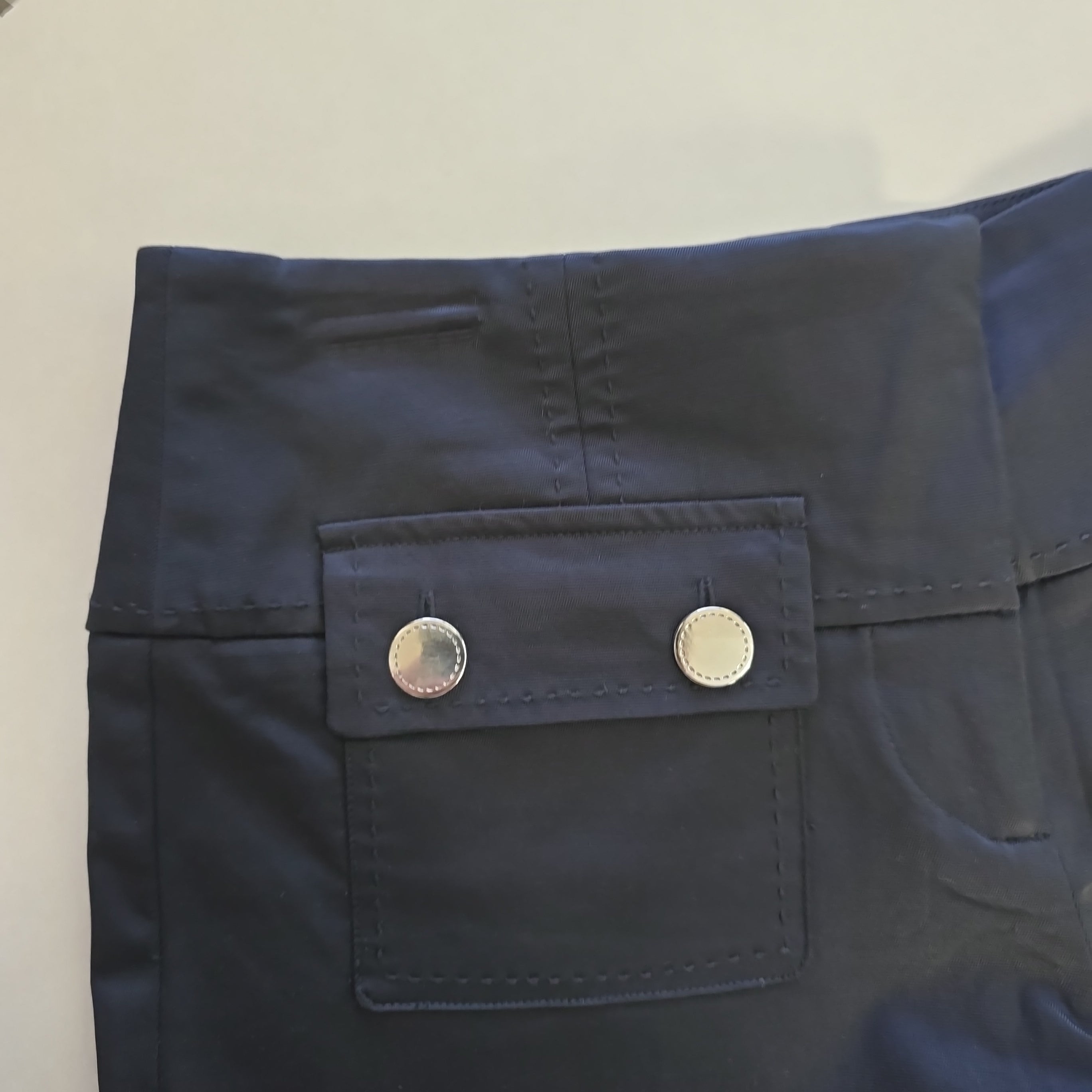 Close-up of a black pants with two buttons on a light beige background