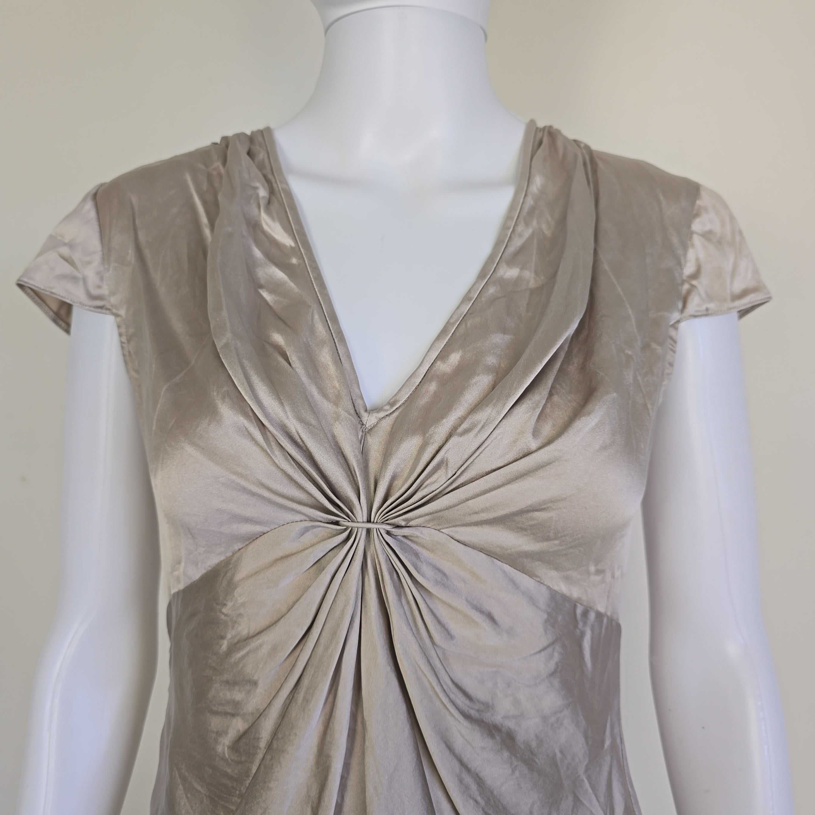 Mannequin wearing a beige top with a pleated design on a plain background