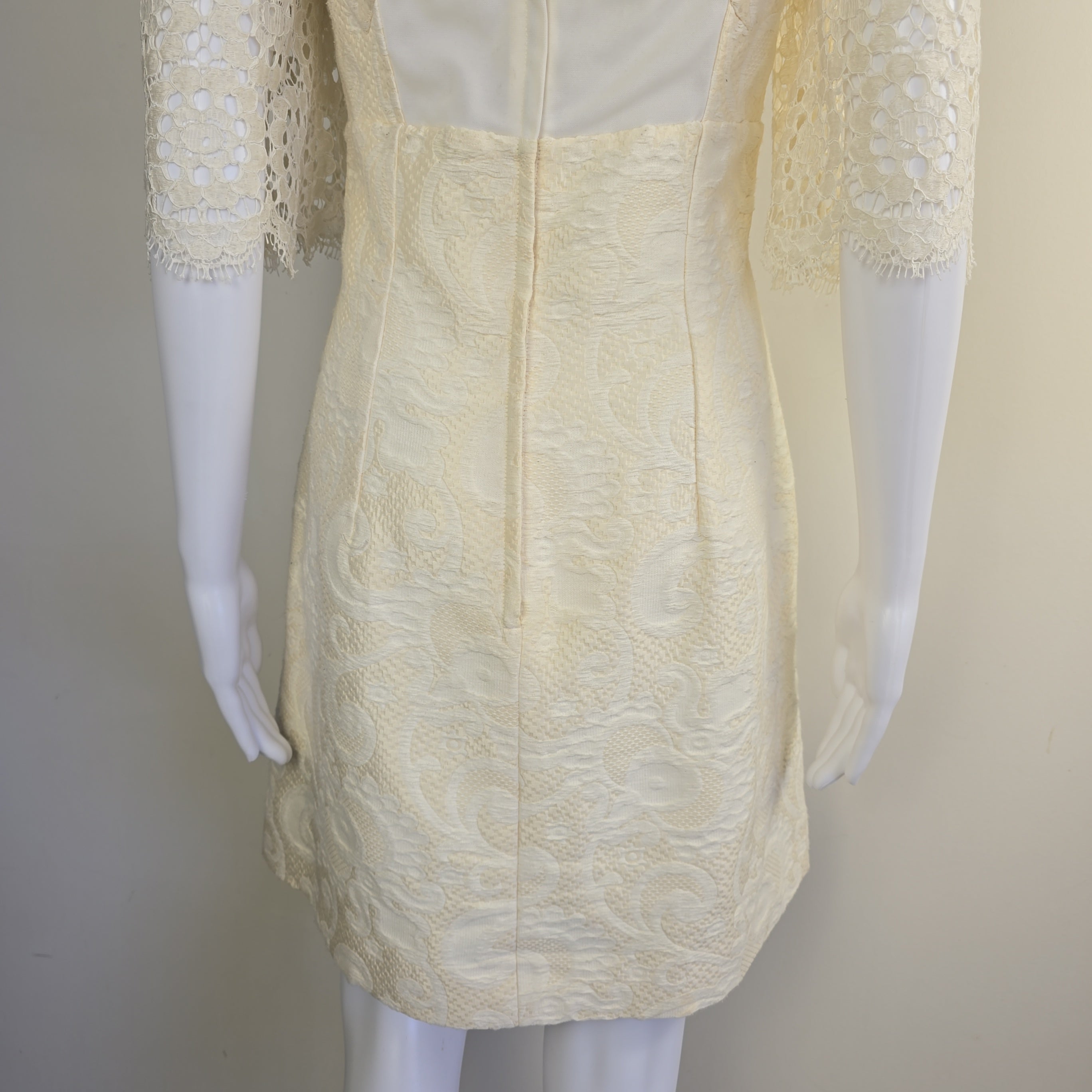 Mannequin wearing a cream-colored lace dress with a plain background
