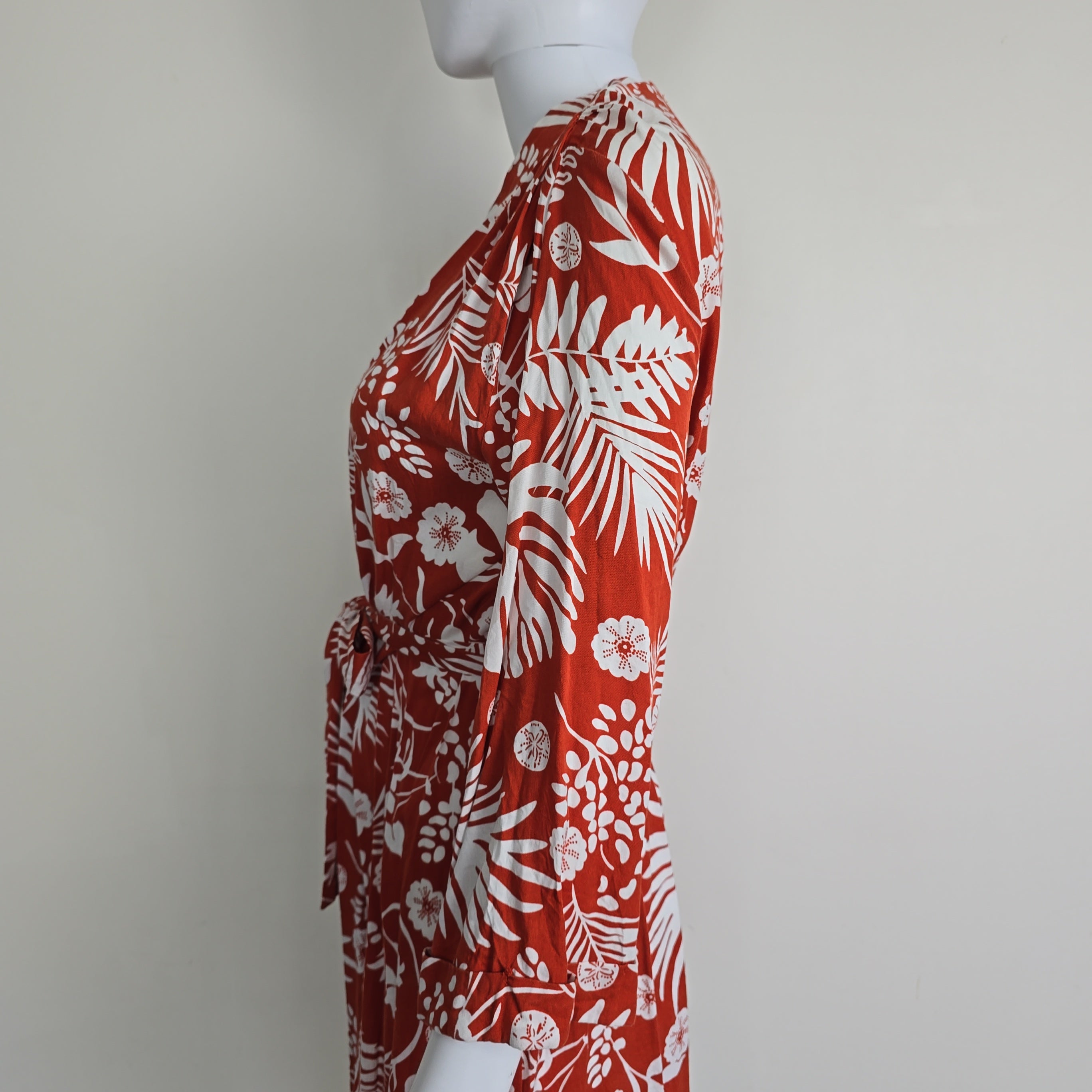 Red fabric with white floral and leaf pattern on a mannequin against a white background