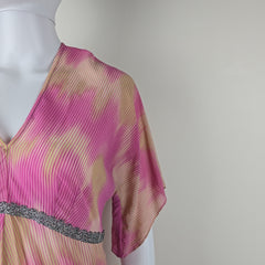 Mannequin wearing a pink and gold pleated garment with a textured edge on a plain background